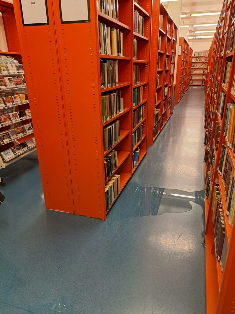 Vesilammikko pääkirjaston kellarin kirjavaraston lattialla kirjahyllyjen keskellä