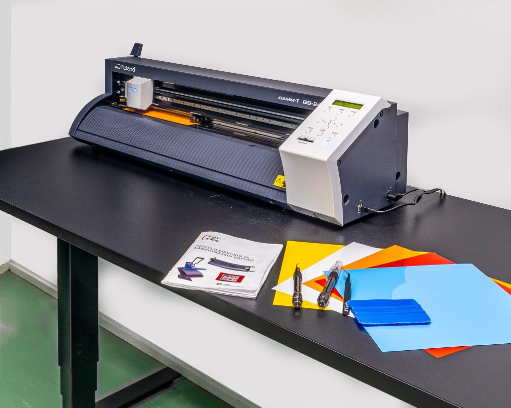 Roland Camm 1 GS-24 vinyylileikkuri ja vinyylikalvoja pöydällä.